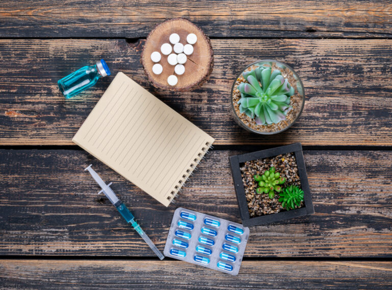 Top-down view of pills, a syringe, a medicine vial, and a notepad arranged on a rustic wooden table with small succulent plants, representing pain management and healthcare alternatives, including the discussion of how **marijuana reduce opioid prescriptions